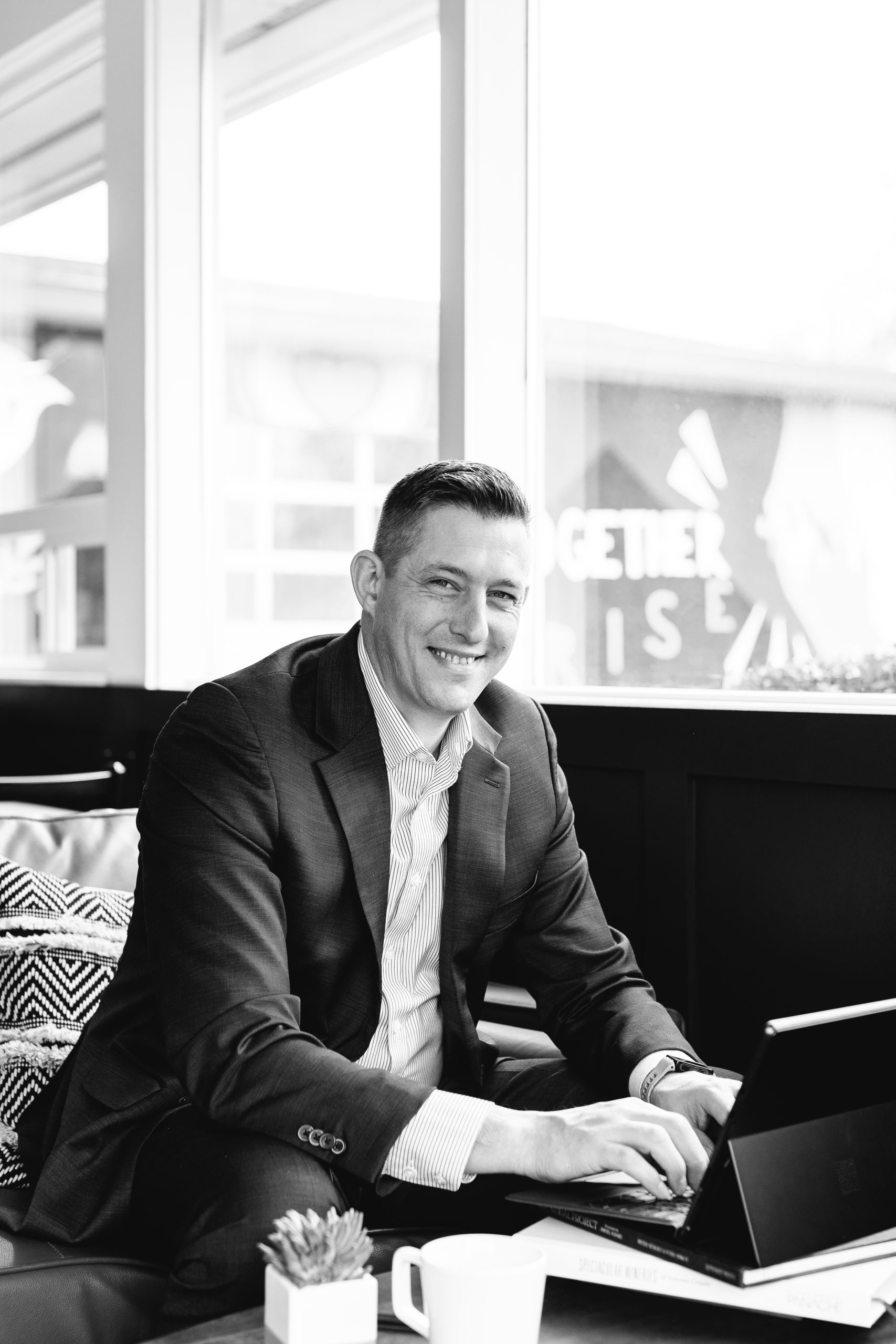 Black and white photo of Realtor Steven Duncan working in a coffee shop. He is looking at the camera and smiling.