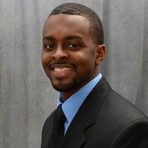 Headshot of Brandon Duncan, Realtor and Owner of Duncan Prime Realty. He is wearing a black suite with a blue dress shirt and black tie. He's looking at the camera and smiling.